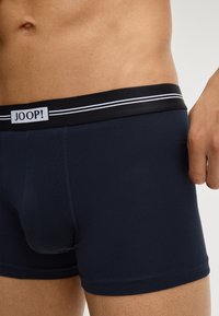Torso maschile che indossa boxer blu navy con elastico nero caratterizzato da strisce bianche e logo "JOOP!" sul davanti.