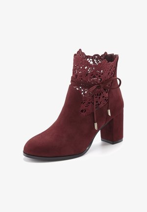Burgundy suede ankle boot featuring a lace overlay at the top, a decorative bow with gold accents, and a chunky heel.