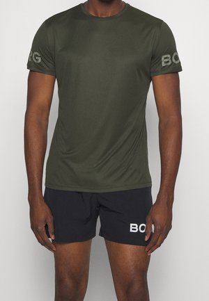 Mann trägt ein olivgrünes kurzärmeliges Hemd und schwarze Shorts mit „BORG“ auf den Ärmeln und der Vorderseite der Shorts.