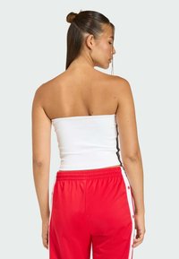 Biela top bez ramienok s priliehavým strihom, skombinovaný s jasne červenými nohavicami so bočnými gombíkmi a pasom na šnúrku. Hladká textúra.