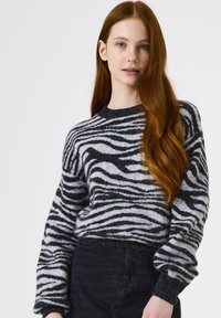 Zwart-wit gestreepte trui van zacht, textuurmateriaal met een ronde hals en geribbelde manchetten, gecombineerd met donkere jeans.