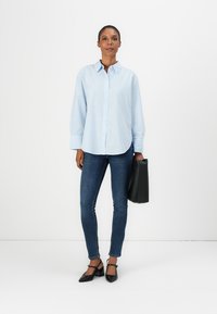 Camicia button-up a righe blu chiaro con vestibilità rilassata, abbinata a jeans skinny blu scuro e ballerine nere a punta, con una borsa nera.