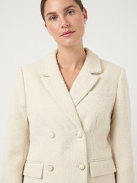 Kreemjas kahekordse nööpimisega jakk tekstuurse kangaga, millel on sälguga krae, kuldsed nööbid ja küljetaskud.