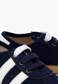 Navy blue suede shoes feature two white horizontal stripes, rounded toe, and white laces with a textured cork sole.