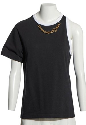 Haut asymétrique noir et blanc à manches courtes avec une manche et un détail chaîne dorée près de l'encolure ronde sur un mannequin.