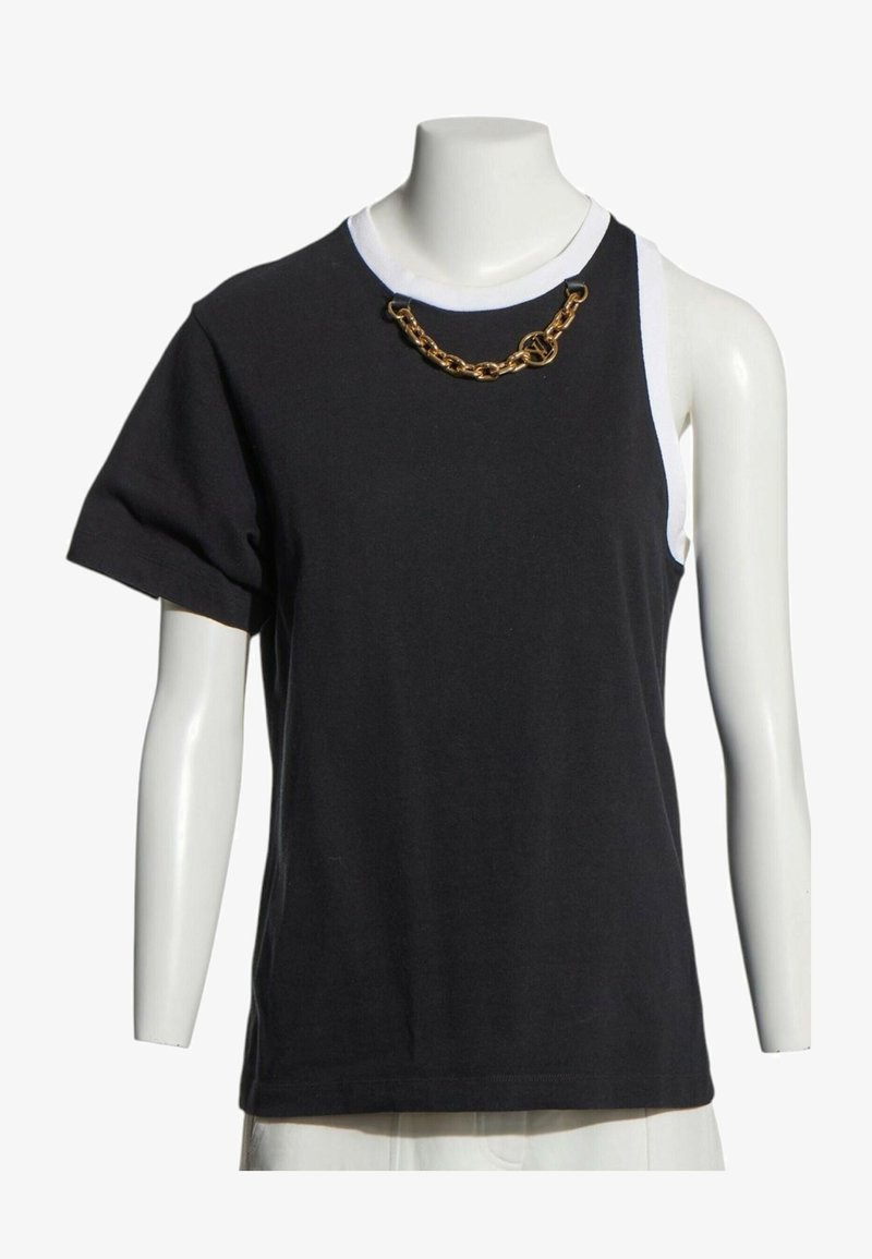 Haut asymétrique noir et blanc à manches courtes avec une manche et un détail chaîne dorée près de l'encolure ronde sur un mannequin.