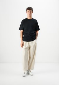 T-shirt de algodão preto com decote redondo e mangas curtas, combinado com calças largas bege e ténis brancos com detalhes coloridos.