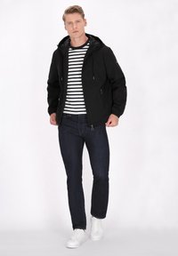 Zwarte hoodie met een gladde textuur, gecombineerd met een wit en zwart gestreept shirt. Donkerblauwe jeans en witte sneakers.