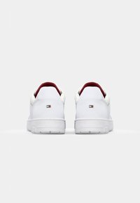 Baskets blanches avec accents rouges, texture en cuir lisse, forme arrondie, col rembourré et semelles en caoutchouc. Logo sur le talon.