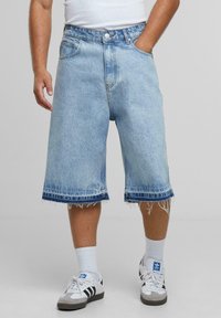 Pantalones cortos de mezclilla azul claro con un corte holgado, dobladillo deshilachado y acentos azul oscuro. Diseño estándar de cinco bolsillos con cierre de botón.