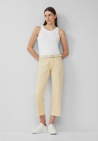 Un débardeur blanc, un pantalon cropped jaune clair avec des ourlets effilochés, et des baskets blanches. Une tenue simple et décontractée au design épuré.