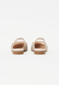 Beige suede sandals with a back strap, flat sole, and circular heel. Smooth texture, minimalistic design, no visible embellishments.