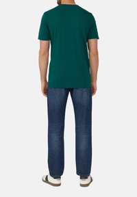 Groene katoenen T-shirt met een ronde hals, korte mouwen en een relaxte pasvorm, gecombineerd met donkerblauwe denimjeans en witte sneakers.