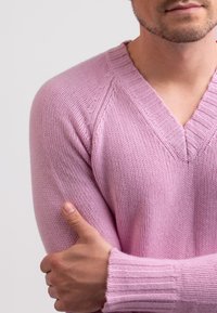 Maglione a maglia rosa chiaro con scollo a V, polsini a costine e un motivo testurizzato. Il tessuto sembra morbido e confortevole.
