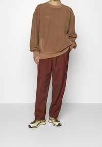 Sudadera de algodón marrón con bordado "HUGO", combinada con pantalones anchos de color óxido y zapatillas beige y amarillas.