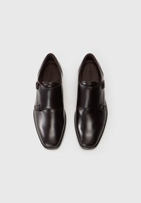 Barna bőr dresszcipők sima felülettel, hegyes orral és oldali csat részletekkel. Minimalista dizájn, elegáns kivitel.