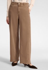 Pantalones de pierna ancha en una tela de color marrón claro con una textura suave. Presenta un bolsillo frontal, pasadores para cinturón y un cierre de botón.