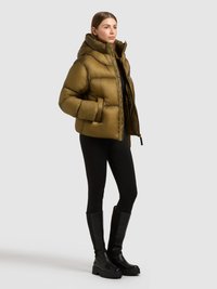 Olíva zöld színű, fényes hatású steppelt dzseki, magas gallérral, cipzáras elülső résszel és két oldalsó zsebbel. Fekete leggingssel és térdig érő csizmával viselve.