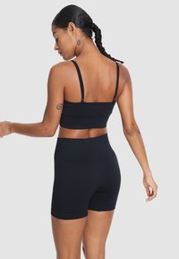 Czarny zestaw sportowy składający się z biustonosza i wysokich spodenek, wykonany z elastycznego materiału. Zawiera cienkie, regulowane ramiączka oraz dopasowany krój.