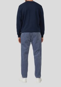 Dunkelblauer Sweatshirt mit langen Ärmeln, kombiniert mit hellblauen Cordhosen. Weiße Sneakers vervollständigen das Outfit. Rückansicht gezeigt.