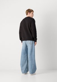 Sweatshirt preto de gola redonda combinado com jeans claros de perna larga. O conjunto apresenta um corte descontraído e um design minimalista. Sapatos brancos.