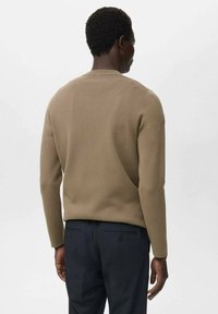 Pull en tricot marron avec un col rond et des manches longues, présentant une texture lisse et un design ajusté, associé à un pantalon bleu marine.