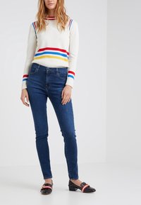 Tröja med vit bas, röda, blå och gula ränder; ihop med mörkblå skinny jeans och svarta skor med röda accenter och nitar.