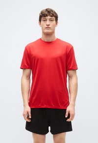 Röd sport-t-shirt med rund halsringning, korta ärmar och en slät textur, kombinerad med svarta shorts. Enkel design utan synliga mönster.