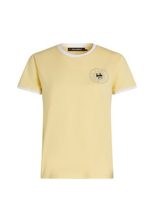 T-shirt jaune à manches courtes avec bordure blanche sur le col et les poignets, présentant un petit logo de chat noir et un texte circulaire sur le côté gauche de la poitrine.