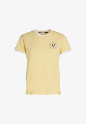 Kollane lühikeste varrukatega T-särk, millel on valge ääristus krae ja varrukate ümber, vasakul rinnal väike must kassi logo ja ümmargune tekst.