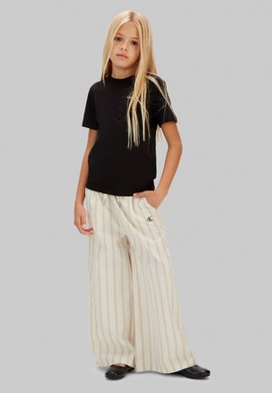 T-shirt nera a maniche corte abbinata a pantaloni larghi crema con righe verticali. I pantaloni hanno una vita con coulisse e dettaglio con logo.
