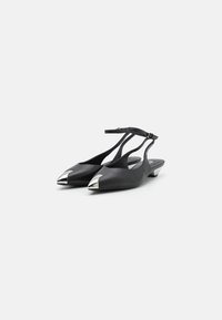Fekete bőr slingback lapos cipők hegyes orral és ezüst színű fémszálakkal az elején. Beállítható boka pánttal és alacsony sarokkal rendelkezik.