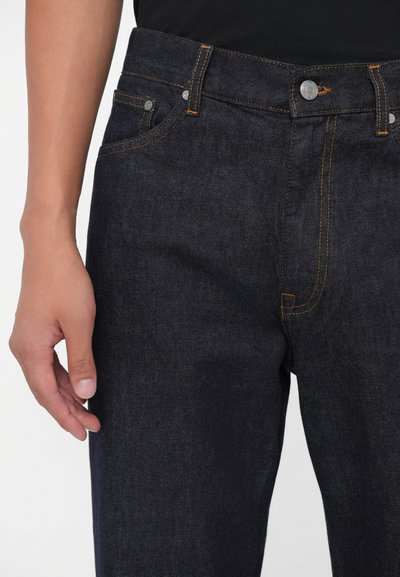 Vaqueros de mezclilla azul oscuro con costuras naranjas, cierre de botón, bolsillos frontales y un diseño ajustado. Textura suave, corte clásico.