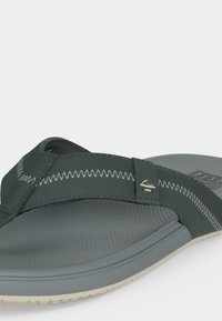 Σανδάλι τύπου φλιπ-φλοπ σε σκούρο γκρι με λευκές ραφές ζιγκ-ζαγκ και υφή στην σόλα, εμφανιζόμενο από κοντινή γωνιακή πλευρική όψη.