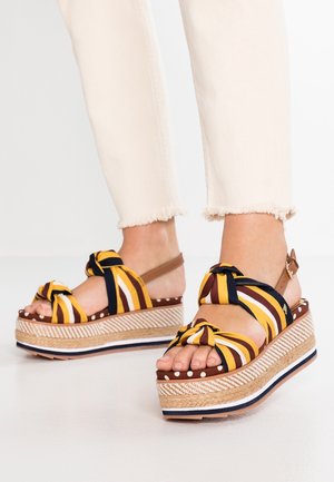 Sandali wedge a strisce con design annodato, in colori giallo, marrone e blu navy, suola in juta e cinturino alla caviglia.
