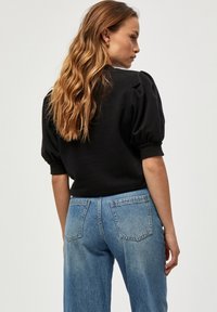 Svart topp med puffärmar, i kombination med ljusblå, högmidjade denimjeans. Synliga bakfickor och en avslappnad passform.