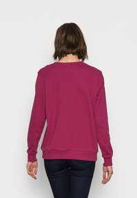 Sudadera ajustada de manga larga en un profundo magenta, con cuello redondo, puños y dobladillo acanalados, hecha de una tela suave y texturizada.