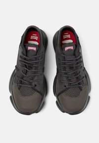 Black athletic shoes featuring a mesh upper, suede accents, rounded toe, and red logo tags on the tongue. Textured and cushioned sole.