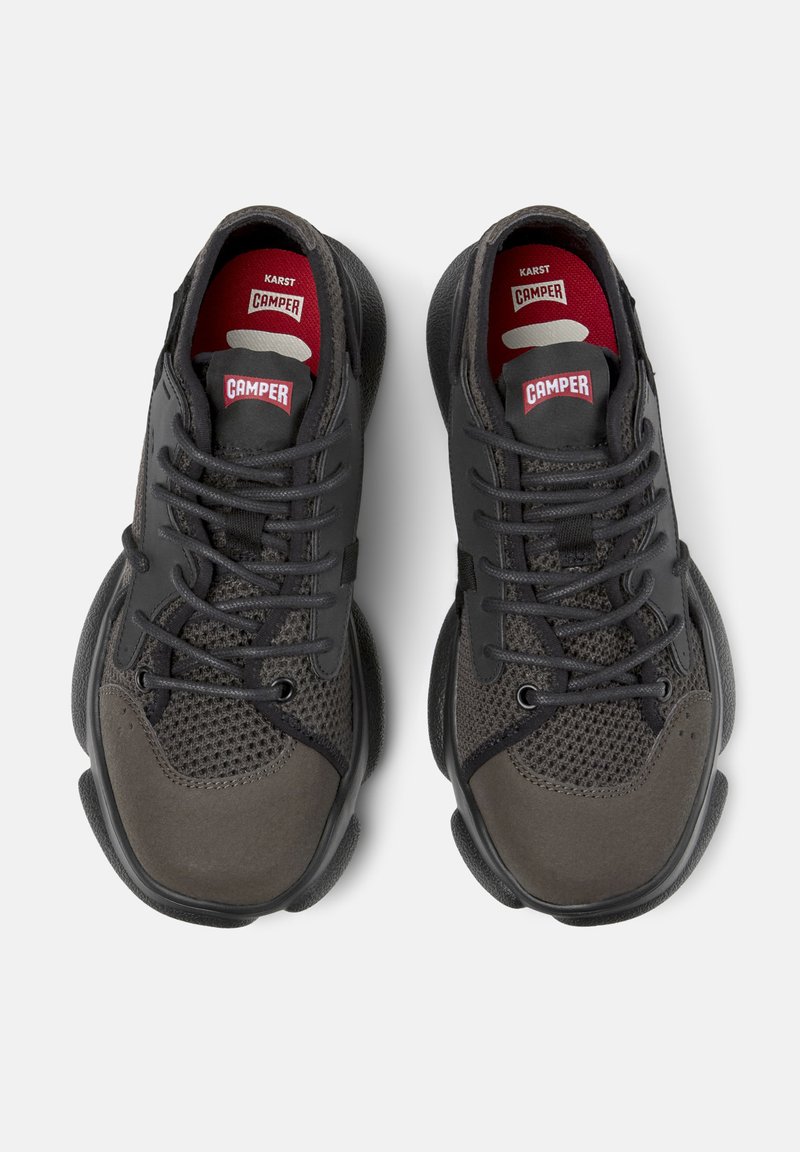 Zapatillas deportivas negras con parte superior de malla, acentos de ante, punta redonda y etiquetas de logo rojas en la lengüeta. Suela texturizada y acolchada.