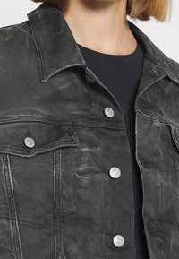 Svart denimjacka med en urtvättad struktur, klassisk krage och silverfärgade tryckknappar. Har bröstfickor och en skräddarsydd passform.