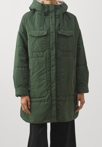 Grön vadderad jacka med huva, som har två bröstfickor, sidofickor med dragkedja och ett mjukt innerfoder. Tyget har en slät yta.