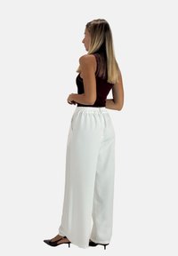 Pantalon blanc à jambes larges avec une taille élastique, associé à un haut bordeaux ajusté. La texture est lisse et la coupe est ample.