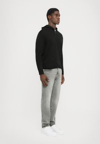 Sort zip-up hoodie i blødt stof, parret med grå jeans og hvide sneakers. Har et strømlinet design med en afslappet pasform.