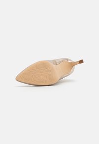 Chaussure à talon haut beige vue de la semelle, montrant un bout pointu, un motif texturé sur la semelle, et un talon fin avec une petite pointe de talon.