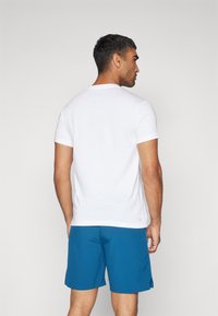 Camiseta blanca de manga corta hecha de algodón, combinada con pantalones cortos azules. La camiseta presenta un cuello redondo y un diseño recto.