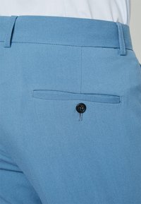 Pantalones azul claro con una textura suave, un bolsillo trasero con un botón negro y líneas limpias y ajustadas.