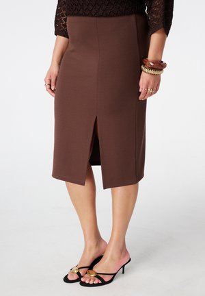 Femme portant une jupe crayon marron mi-longue avec une fente devant, des sandales à talons noires et des bracelets à son poignet droit.