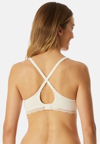 Bra bianco con pizzo, spalline incrociate regolabili e chiusura a gancio e o occhiello sul retro. Tessuto liscio con una consistenza morbida.