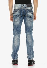 Verwaschene blaue Denim-Jeans mit geradem Schnitt. Zu den Merkmalen gehören Kontrastnähte, aufgesetzte Taschen und ein strukturierter Bund.