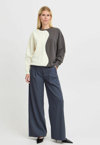 Color-blocked sweatshirt in cream and dark gray, oversized fit. Paired with navy pinstriped wide-leg trousers and black pointed shoes.
